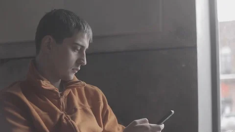 Young man using smartphone sitting by window in cafe Stock Footage 91700297