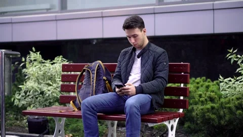 Young Man Using Smartphone sitting on bench in the street Stock Footage 97849938