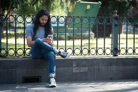 Young man using smartphone sitting on park ledge Stock Photos