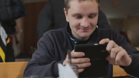 Young man using smartphone, smiling and talking with someone. Cafe interior Video stock 74434401