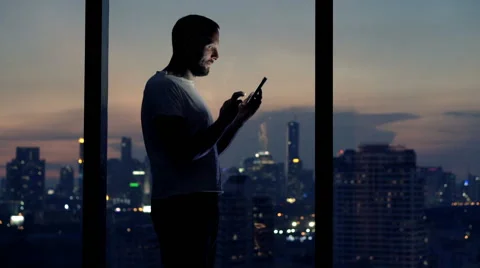 Young man using smartphone standing by window at night Stock Footage 62220428