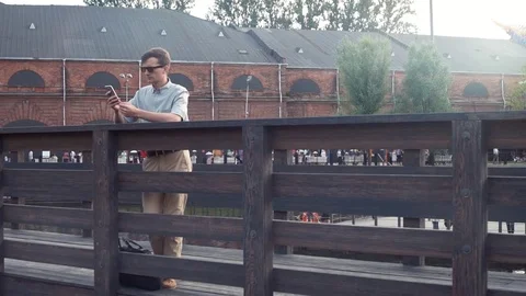 Young man using smartphone standing on a wooden bridge. City park at background. Stock Footage 79357062