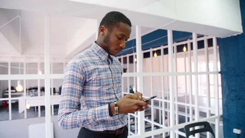 Young man is using smartphone, standing in modern office. Video stock 82736801