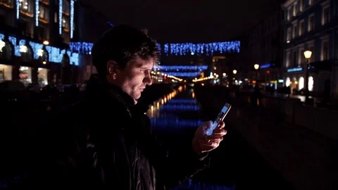Young man using smartphone standing alone outdoors at night on busy city street Stock Footage 83629786
