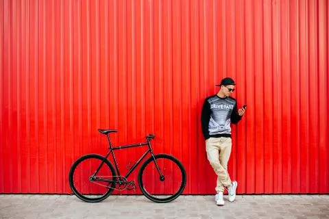 Young man using a smartphone, standing near the bike, outdoors. Stock Photos
