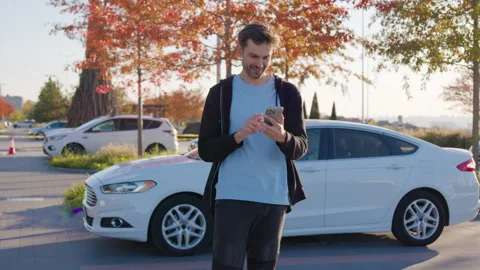 Young man using smartphone to unlock carsharing vehicle, preparing for urban Stock Footage 316835428