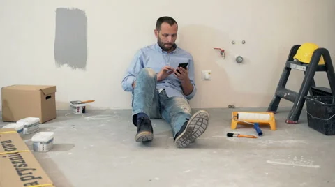 Young man using smartphone while sitting on floor at his new home Stock Footage 63994412