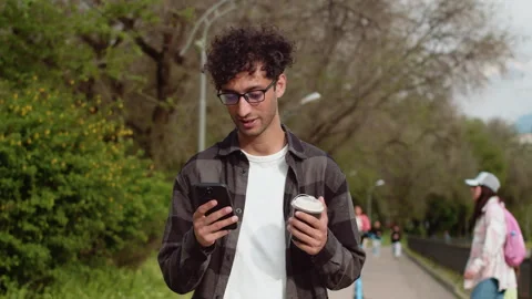 Young man using smartphone while walking in a park Stock Footage 287512757