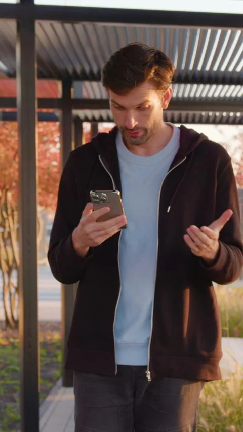 Young man using smartphone while walking through modern outdoor space with Stock Footage 318474539