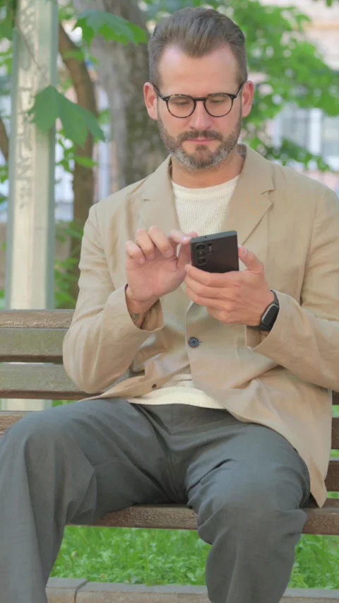 Young Man Using Smartphone while Sitting Outdoor, Vertical Video Stock Footage 319017936