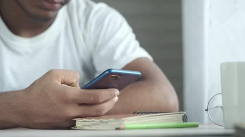 Young man using smartphone while sitting at desk with notebook and pencil i.. Stock Footage 332623290