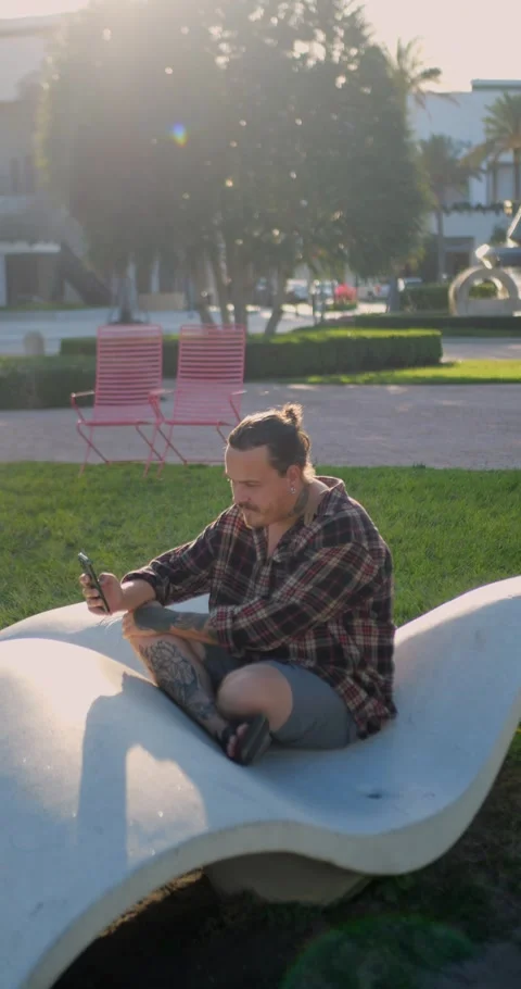 Young Man Using Smartphone While Sitting On Modern Outdoor Bench... Stockbeeldmateriaal 333525121