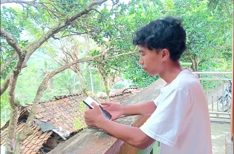 Young man using a smartphone while leaning on a front house wall. 스톡 동영상 335019070