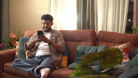 Young man using smartphone while sitting on sofa Stock Footage 338400820