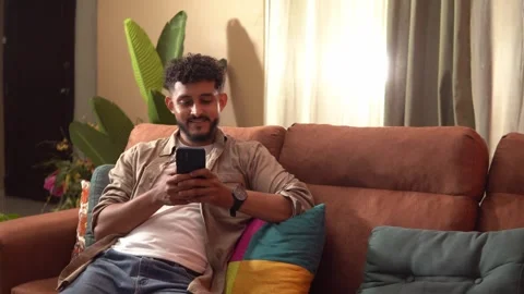 Young man using smartphone while relaxing on sofa Stock Footage 338401026