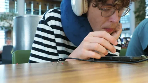 Young man using smartphone while wearing neck pillow at airport Stock Footage 346378910
