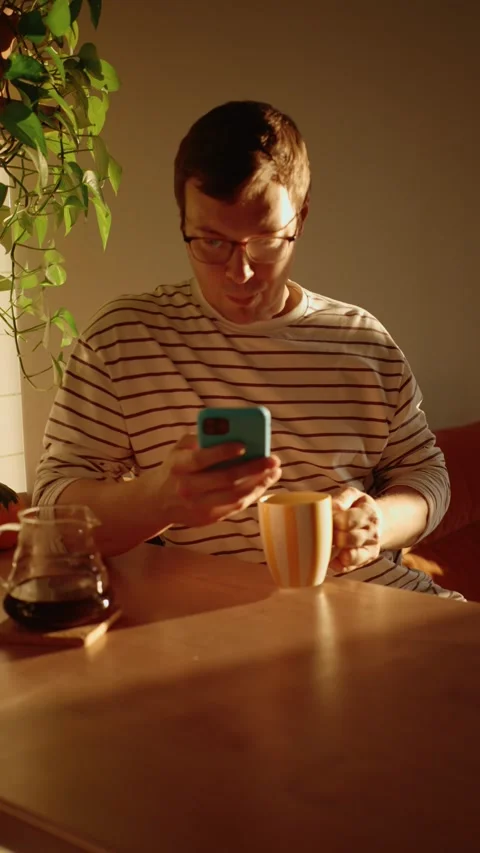 Young man using smartphone while drinking coffee at home in the morning Stock Footage 346522311