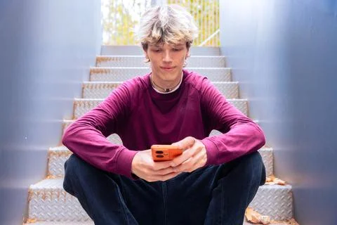 Young Man Using Smartphone While Sitting on Metal Stairs Outdoors Stock Photos