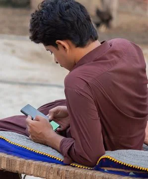 Young man using smartphone while sitting on traditional cot outdoors Stock Photos