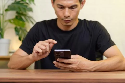 Young Man Using Smartphone While Seated at Table in Modern Setting Stock Photos