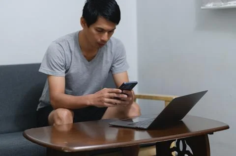Young Man Using Smartphone While Sitting at a Table with Laptop Foto stock