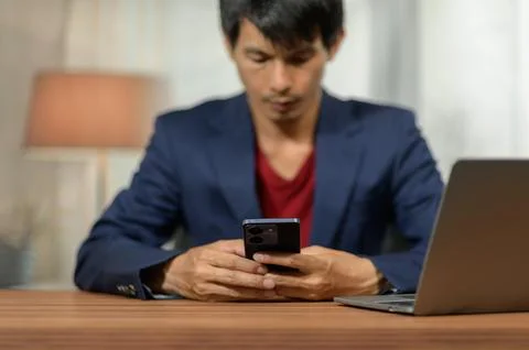 Young Man Using Smartphone in Workspace with Laptop and Interior Background Stock Photos