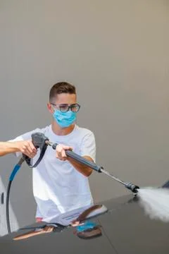 Young man using a surgical mask and washing a car with a high pressure water  Stock Photos