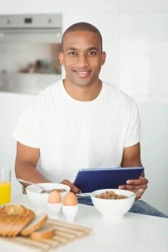 Young man using tablet and eating breakfast in kitchen Stock-Fotos