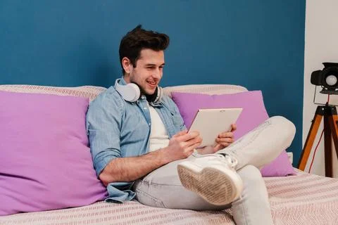 Young man using a tablet app to browse on internet sitting at home couch. Male Foto stock
