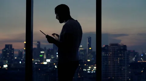 Young man using tablet computer standing by window at night Stock Footage 62221112