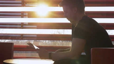 Young man using a tablet computer sitting against the sun Stock Footage 73884384