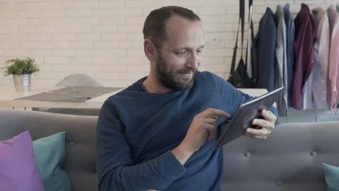 Young man using tablet computer while sitting on sofa at home Video stock 74730775