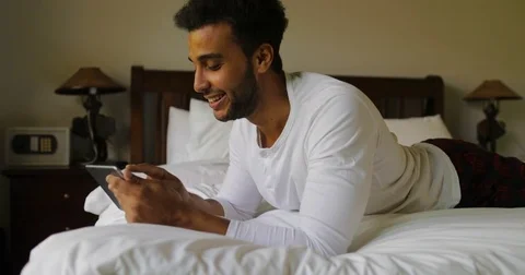 Young Man Using Tablet Computer Lying On Bed Happy Smiling Hispanic Guy Chatting Stock Footage