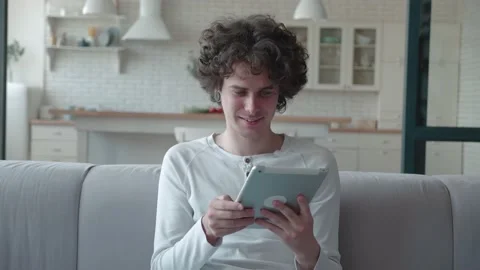 Young man using tablet computer while sitting on the sofa at home. Hipster with Stock Footage 160252749