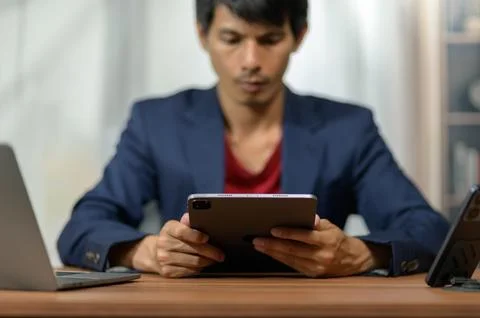 Young Man Using Tablet Computer at Office Desk with Laptop and Smartphone Stockfoto's