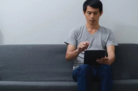Young Man Using Tablet on Couch in Minimalist Room Stock Photos