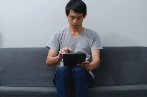 Young Man Using Tablet on Couch in Comfortable Indoor Setting 스톡 사진