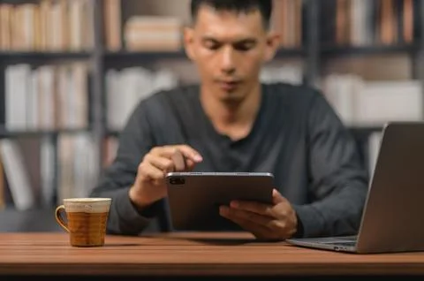 Young Man Using Tablet at Desk in Library with Books in Background Stock Photos