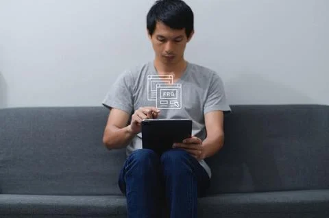 Young Man Using Tablet with FAQ Icon on Gray Sofa Stockfoto's