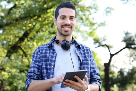 Young man using tablet with headphones in park. Stock Photos