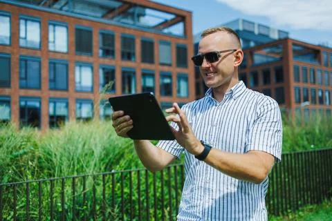 Young man using tablet outside modern building in city on sunny day Stock Photos