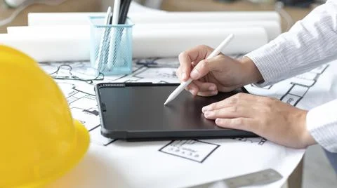 Young man using tablet plotting a system of building structures in blueprints Fotos de archivo