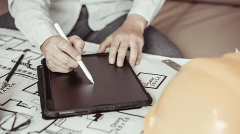 Young man using tablet plotting a system of building structures in blueprints Stock Photos
