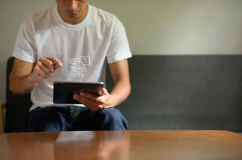 Young Man Using Tablet with Question Mark Icon on Shirt in Casual Setting Stock Photos