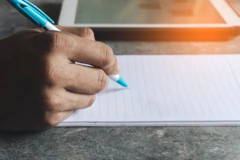 Young man using a tablet to study online at home with a note book on the table Stock Photos