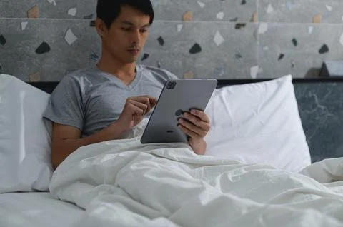 Young Man Using Tablet While Relaxing in Cozy Bed Setting Stock Photos