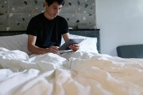 Young man using tablet while relaxing on comfortable bed in room Stock Photos