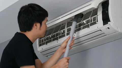 Young man using vacuum cleaner to cleaning the air conditioner at home Stock Footage 155343377