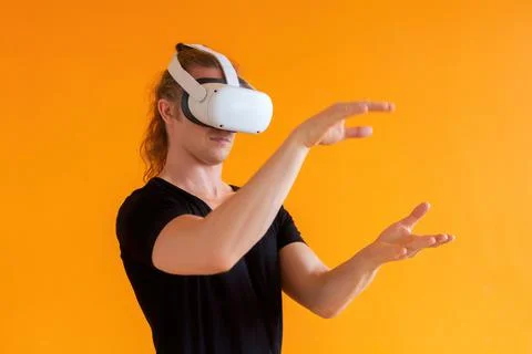Young man using virtual reality headset. Isolated on orange background. Stock Photos
