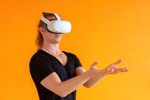 Young man using virtual reality headset. Isolated on orange background. Stock Photos